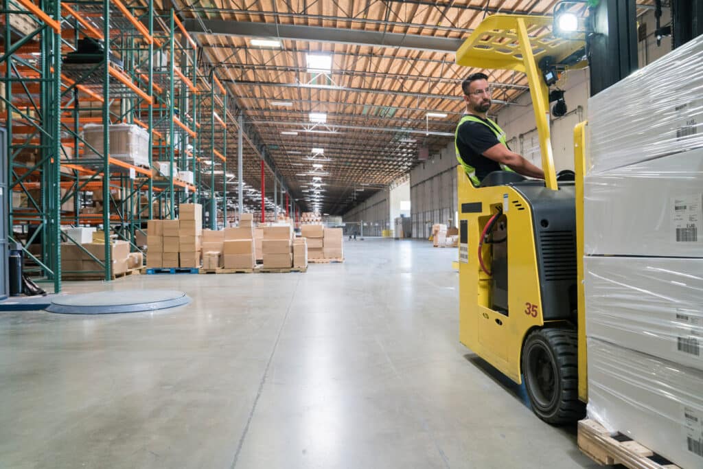 Warehouse worker  using a forklift to move boxes in a wharehouse.
